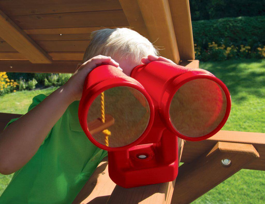 Kid with green shirt looking out of Big Red Binoculars, an imaginative accessory on a Rainbow Play outdoor wooden playset. 
